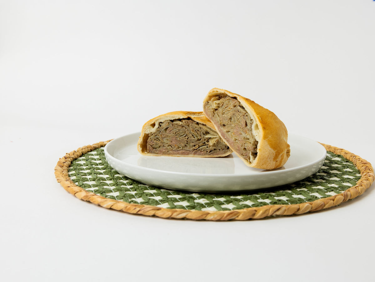 A Lehto's beef pasty cut in half on a white plate, showing the beef, potato, rutabaga and onion filling.
