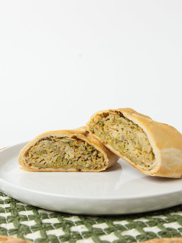 A Lehto's broccoli cheddar pasty cut in half, showing the broccoli and cheddar filling inside the golden crust.