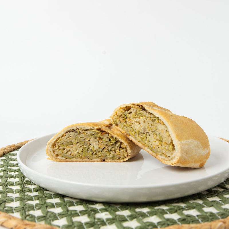 A Lehto's broccoli cheddar pasty cut in half, showing the broccoli and cheddar filling inside the golden crust.