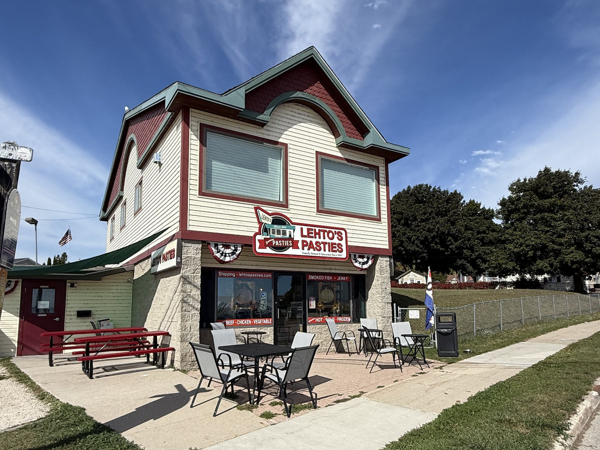 Lehto's Pasties downtown store in St. Ignace seen from the corner, with patio tables and red picnic tables beside the building.