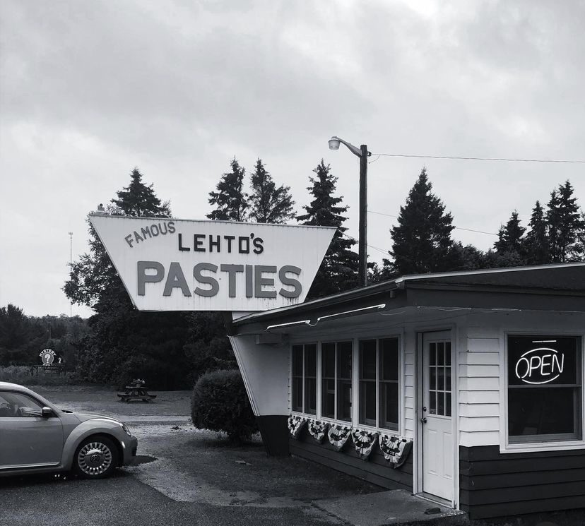 The original Lehto's Pasties stand on US-2 in black and white, under its angular roadside sign.